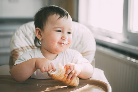 baby in the kitchen eagerly eating the delicious cream horns, filled with a vanilla creamの写真素材