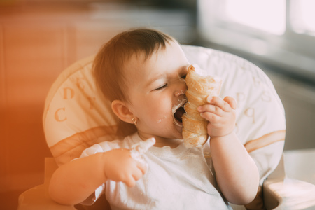 baby in the kitchen eagerly eating the delicious cream horns, filled with a vanilla creamの写真素材