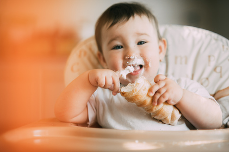 baby in the kitchen eagerly eating the delicious cream horns, filled with a vanilla creamの写真素材