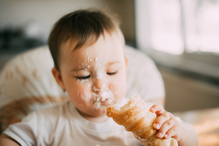 baby in the kitchen eagerly eating the delicious cream horns, filled with a vanilla creamの写真素材