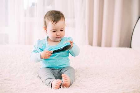 little girl with a blue comb in a blue jacket on the bedの写真素材