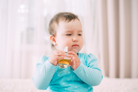 Beautiful little girl in a blue jacket with perfume in her handsの写真素材