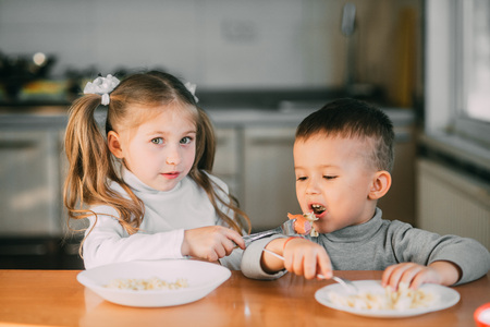Boy and girl children in the kitchen eating sausages with pasta is very fun and friendlyの写真素材