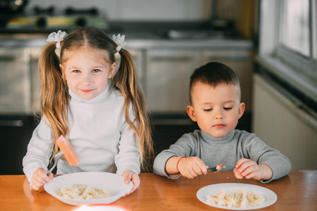 Boy and girl children in the kitchen eating sausages with pasta is very fun and friendlyの写真素材