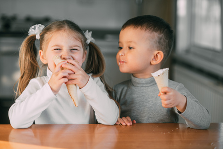 kids boy and girl eating ice cream cone in the kitchen is a lot of funの写真素材