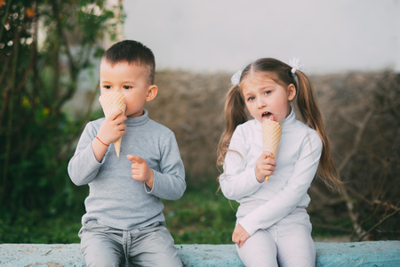 Kids Boy and girl eating ice cream outdoors on grass and trees backgroundの写真素材