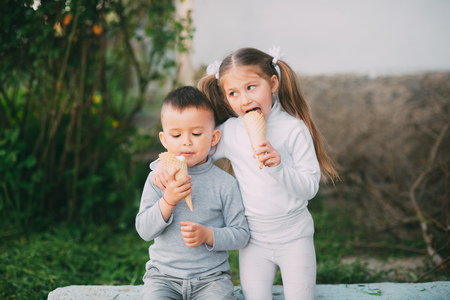 Kids Boy and girl eating ice cream outdoors on grass and trees backgroundの写真素材