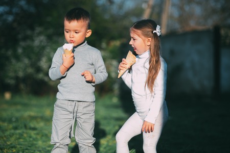 Kids Boy and girl eating ice cream outdoors on grass and trees backgroundの写真素材