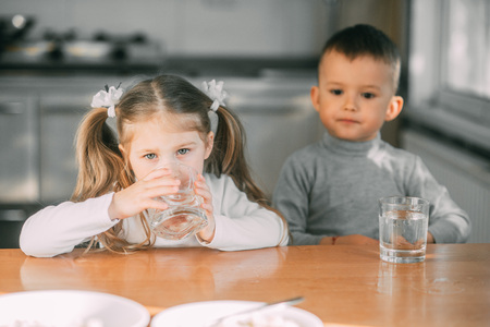 Children boy and girl in the kitchen drinking water from glassesの写真素材