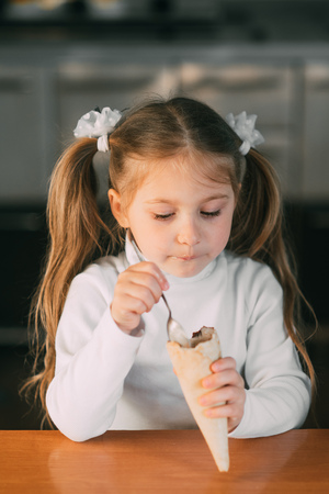 The girl in the kitchen eating the ice-cream cone with a spoon the light of dayの写真素材