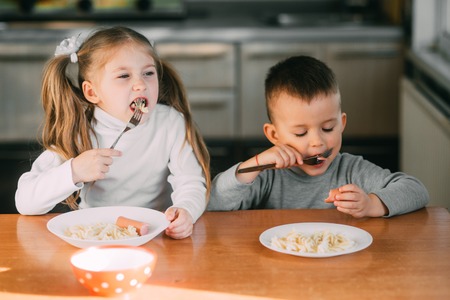 Boy and girl children in the kitchen eating sausages with pasta is very fun and friendlyの写真素材