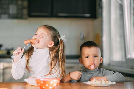 Boy and girl children in the kitchen eating sausages with pasta is very fun and friendlyの写真素材