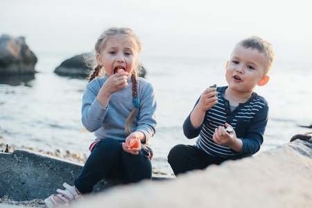 children , girl and boy eating tomato and cucumber on the background of the sea togetherの写真素材