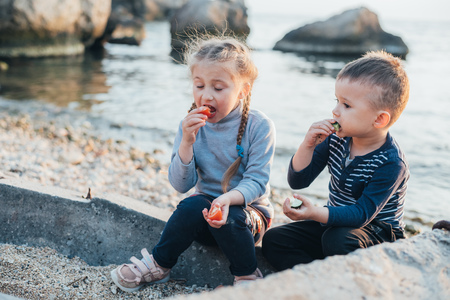 children , girl and boy eating tomato and cucumber on the background of the sea togetherの写真素材