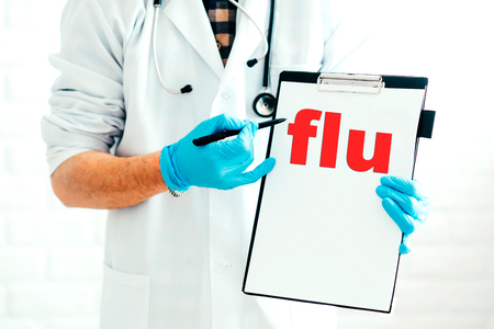 Doctor with clipboard on a white background with a pen shows the name of the disease flu Written in redの写真素材