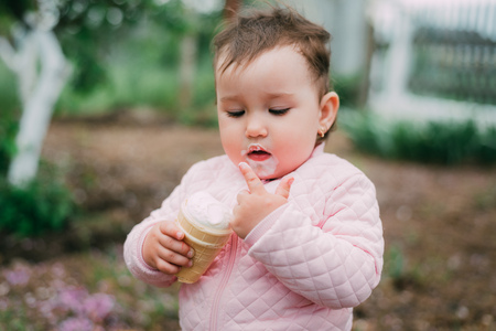 little girl in the garden on the background of greenery and trees very cute eating ice cream finger in a waffle Cup dirty faceの写真素材