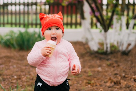 little girl in the garden in a red hat eating ice cream in a waffle Cup