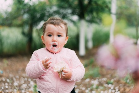 little girl in the garden on the background of greenery and trees very cute eating ice cream finger in a waffle Cup dirty faceの写真素材