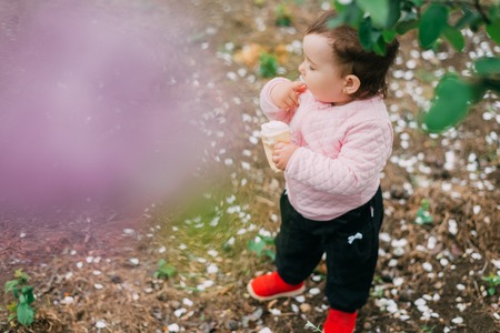 little girl in the garden on the background of greenery and trees very cute eating ice cream finger...