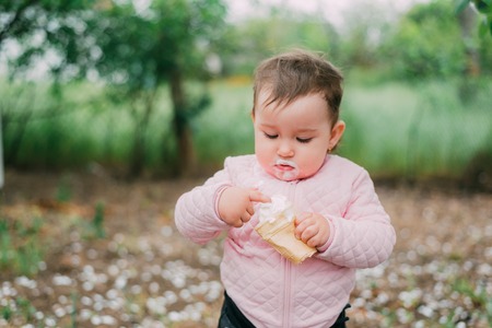 little girl in the garden on the background of greenery and trees very cute eating ice cream finger in a waffle Cup dirty faceの写真素材