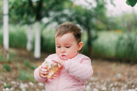 little girl in the garden on the background of greenery and trees very cute eating ice cream finger in a waffle Cup dirty faceの写真素材