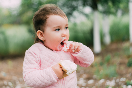 little girl in the garden on the background of greenery and trees very cute eating ice cream finger in a waffle Cup dirty faceの写真素材