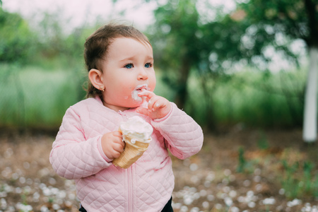 little girl in the garden on the background of greenery and trees very cute eating ice cream finger in a waffle Cup dirty faceの写真素材