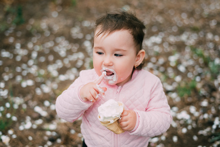 little girl in the garden on the background of greenery and trees very cute eating ice cream finger in a waffle Cup dirty faceの写真素材