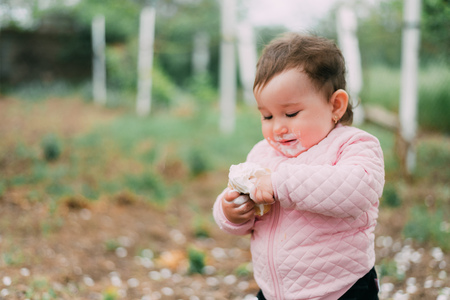 little girl in the garden on the background of greenery and trees very cute eating ice cream finger in a waffle Cup dirty faceの写真素材