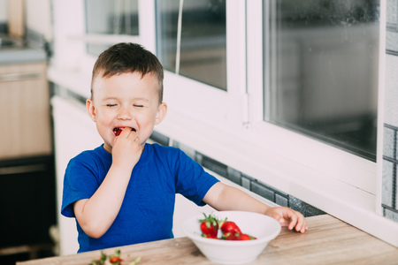 A child, a boy in the kitchen eating strawberries very appetizing and tasty, stocked with vitaminsの写真素材
