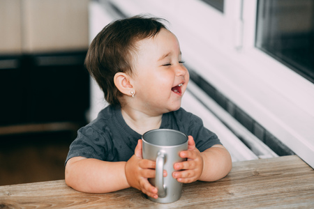 A little girl in the kitchen drinking water from a silver mug very greedily, thirstyの写真素材