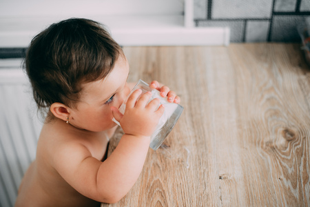 A little girl in the kitchen drinking milk, milkshake or yogurt from a glass is very appetizing and...