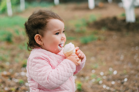 little girl in the garden on the background of greenery and trees very cute eating ice cream in a waffle Cup dirty faceの写真素材