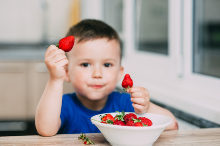 A child, a boy in the kitchen eating strawberries very appetizing and tasty, stocked with vitaminsの写真素材