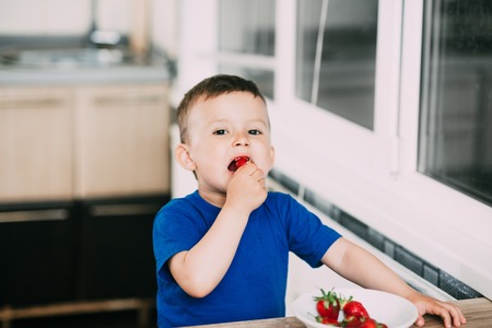 A child, a boy in the kitchen eating strawberries very appetizing and tasty, stocked with vitaminsの写真素材