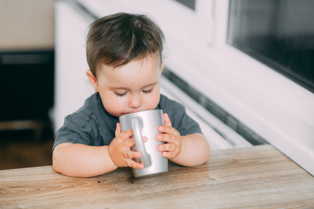 A little girl in the kitchen drinking water from a silver mug very greedily, thirstyの写真素材