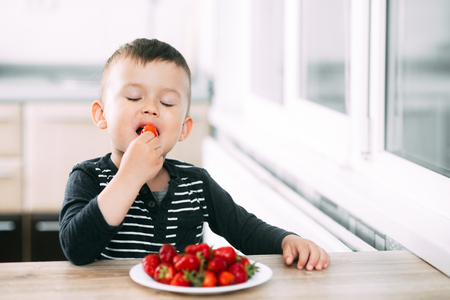 Little boy in the kitchen eating fresh strawberries very appetizing and tastyの写真素材