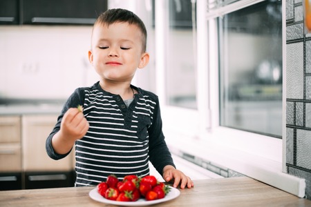 Little boy in the kitchen eating fresh strawberries very appetizing and tastyの写真素材