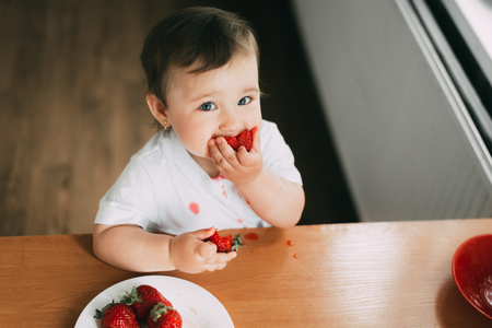 Little girl child in white t-shirt eating strawberries all smeared and dirty very funnyの写真素材