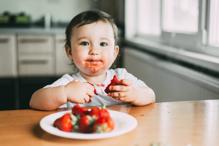 Little girl child in white t-shirt eating strawberries all smeared and dirty very funny