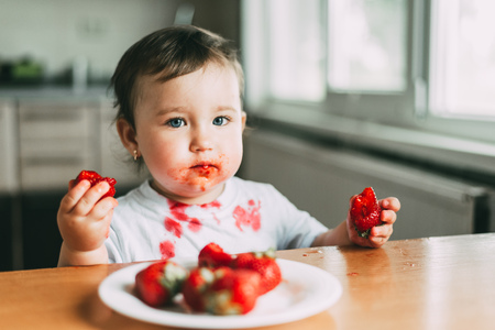 Little girl child in white t-shirt eating strawberries all smeared and dirty very funnyの写真素材