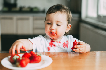 Little girl child in white t-shirt eating strawberries all smeared and dirty very funnyの写真素材