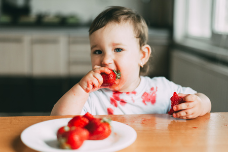 Little girl child in white t-shirt eating strawberries all smeared and dirty very funny