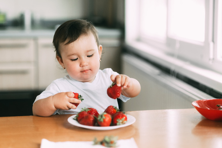 Little girl child in white t-shirt eating strawberries all smeared and dirty very funnyの写真素材