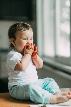 A little girl child in a white t-shirt climbed on the table sitting and eating strawberriesの写真素材