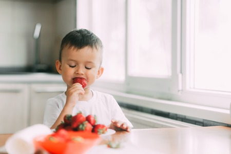 a charming child in a white t-shirt eats fresh homemade strawberries from the gardenの写真素材
