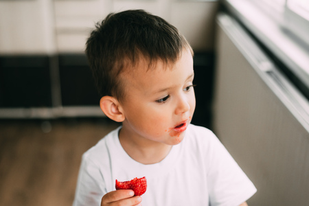 a charming child in a white t-shirt eats fresh homemade strawberries from the gardenの写真素材