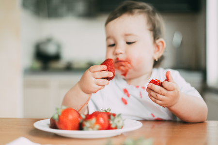 Little girl child in white t-shirt eating strawberries all smeared and dirty very funnyの写真素材