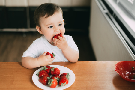 Little girl child in white t-shirt eating strawberries all smeared and dirty very funnyの写真素材