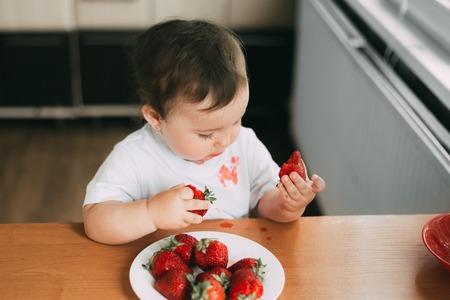 Little girl child in white t-shirt eating strawberries all smeared and dirty very funnyの写真素材